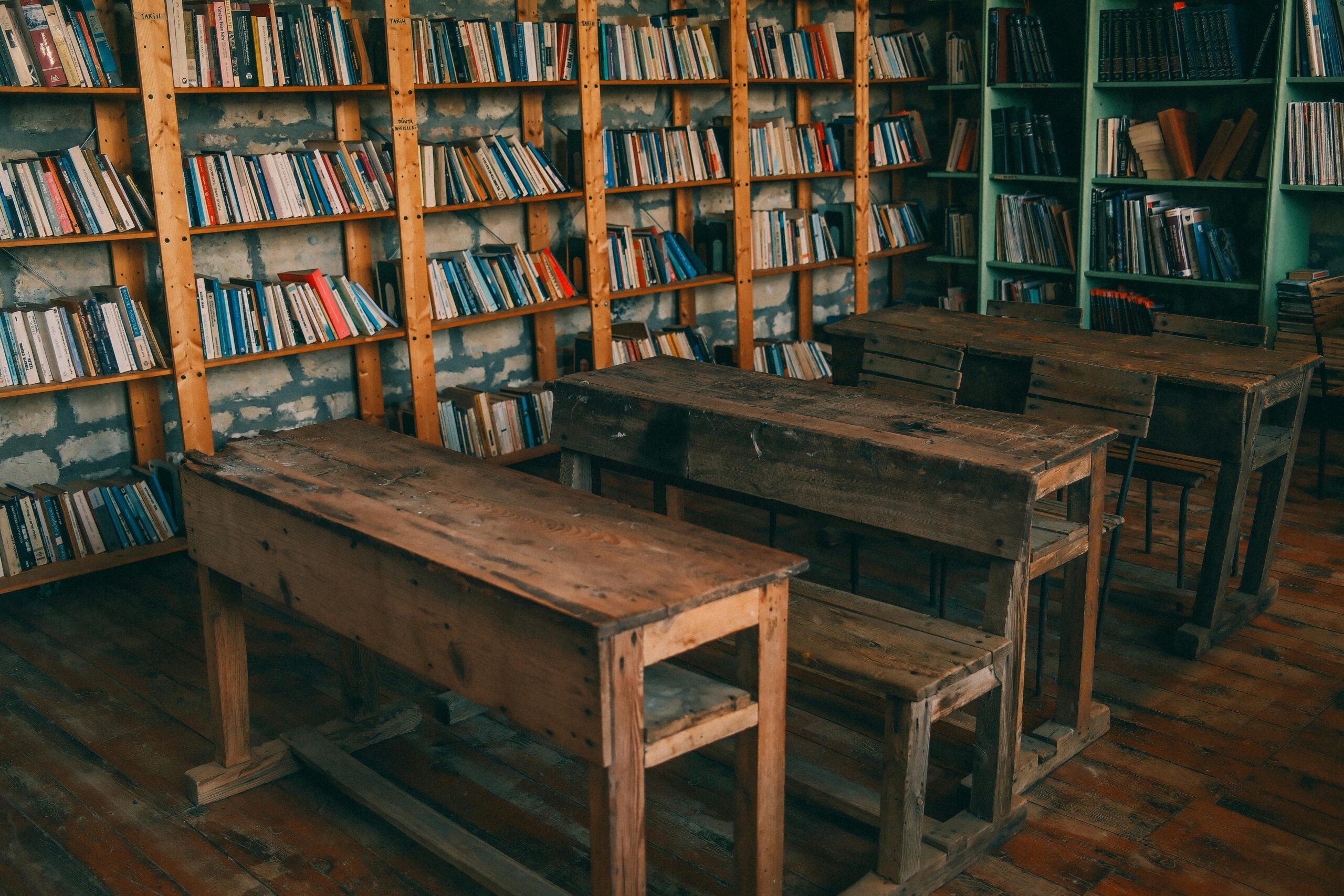 Rustic classroom featuring wooden desks and bookshelves filled with books.