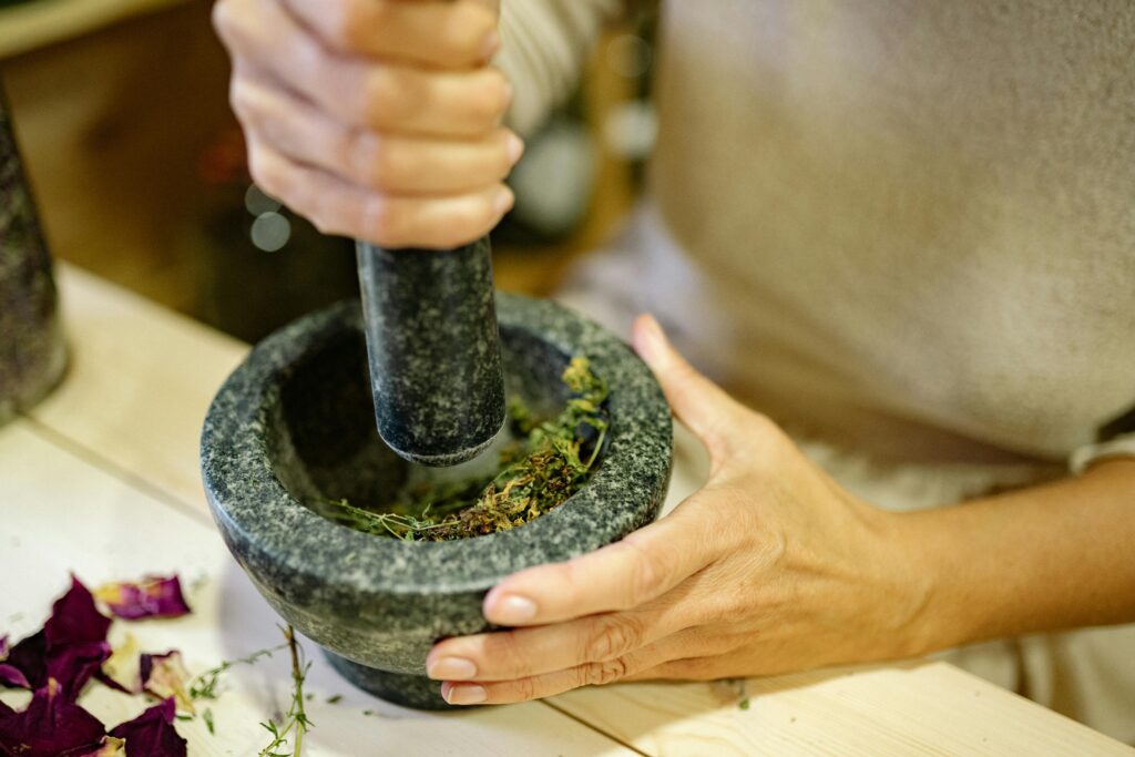 Hands using a mortar and pestle to grind herbs, showcasing culinary preparation.