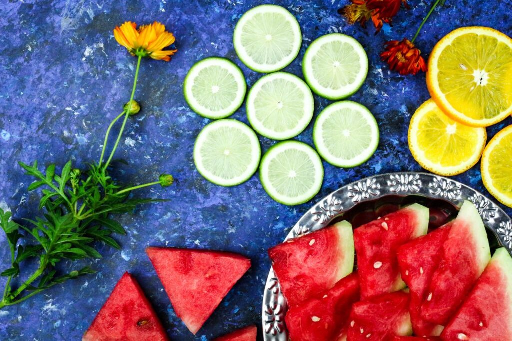 Colorful arrangement of fruits and flowers on a blue textured background, perfect for summer themes.